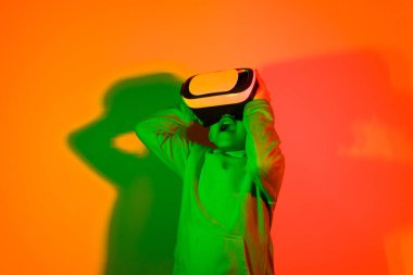 a child surprised with the technology provided by virtual reality glasses standing in front of a background colored by neon lights. High quality photo