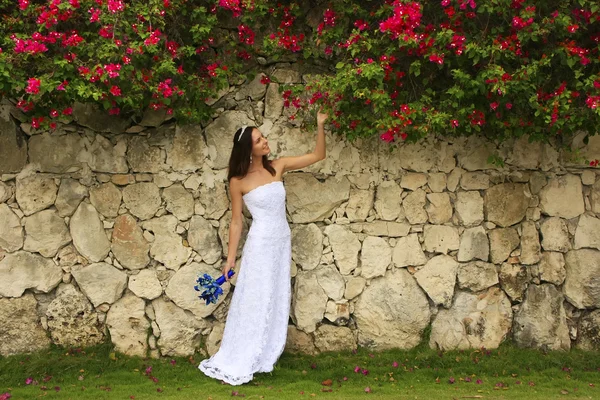 Jovem mulher em vestido de noiva posando na frente da parede de pedra w — Fotografia de Stock