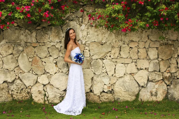 Jovem mulher em vestido de noiva posando na frente da parede de pedra w — Fotografia de Stock