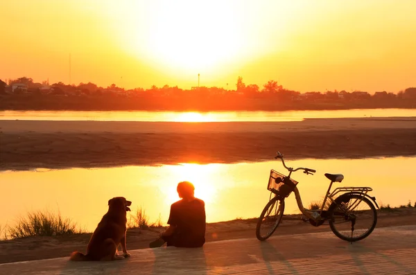 Silhouette Mann mit Hund beobachtet Sonnenuntergang am Wasser des Mekong — Stockfoto