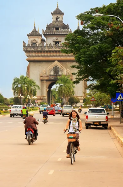 Young woman riding bike near Victory Gate Patuxai, Vientiane, La — Stock Photo, Image