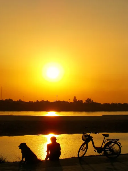 Hombre silueta con un perro mirando el atardecer en el agua del río Mekong — Foto de Stock