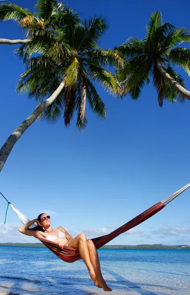 Jonge vrouw in bikini zittend in een hangmat tussen palmbomen, o — Stockfoto