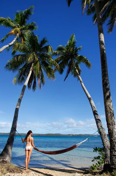 Mujer joven en bikini parada junto a la hamaca entre palmeras —  Fotos de Stock