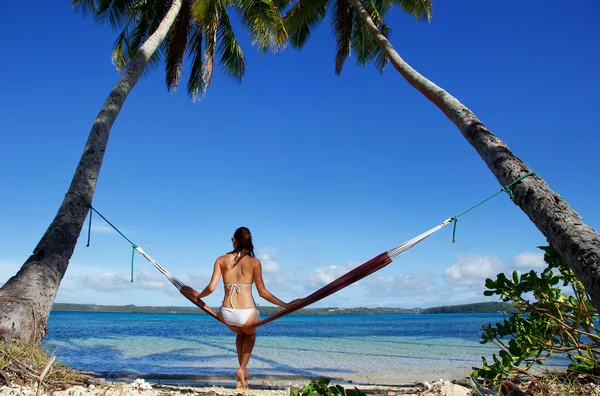 Młoda kobieta w bikini siedzi w hamaku pomiędzy palmami, o — Zdjęcie stockowe