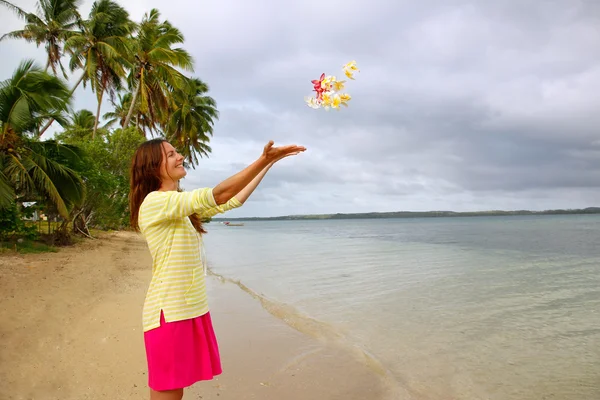 Junge Frau am Strand wirft Blumen in die Luft — Stockfoto