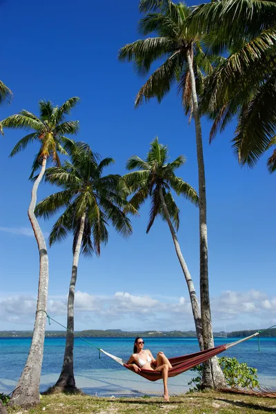 Ung kvinna i bikini som sitter i en hängmatta mellan palmerna, o — Stockfoto