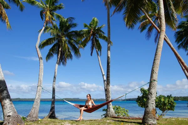 Ung kvinna i bikini som sitter i en hängmatta mellan palmerna, o — Stockfoto