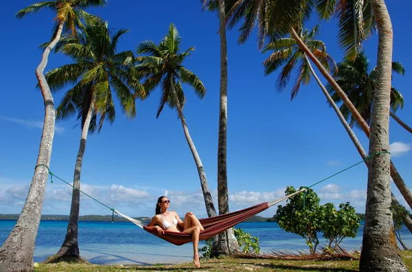 Ung kvinna i bikini som sitter i en hängmatta mellan palmerna, o — Stockfoto