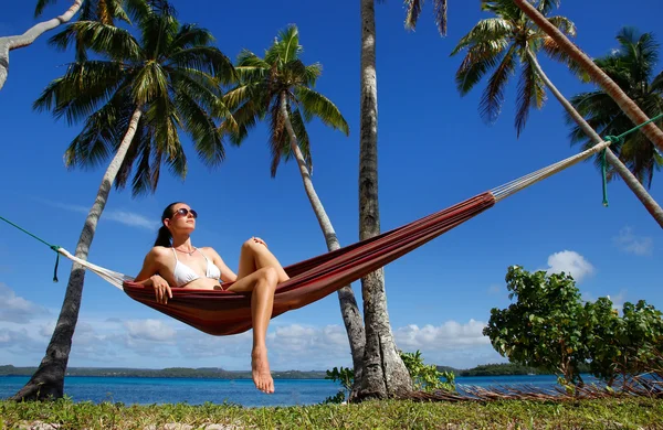 Ung kvinna i bikini som sitter i en hängmatta mellan palmerna, o — Stockfoto