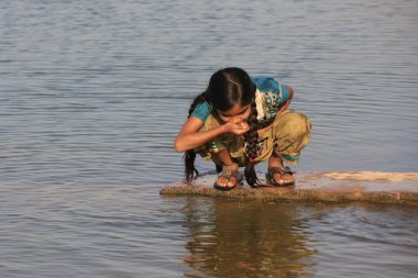 Local girl drinking from water reservoir, Khichan village, India clipart