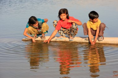 Local kids drinking from water reservoir, Khichan village, India clipart