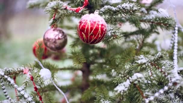 Kerstboom met speelgoed op een winterdag buiten. Sneeuw valt en bedekt de takken. Oudejaarsavond — Stockvideo