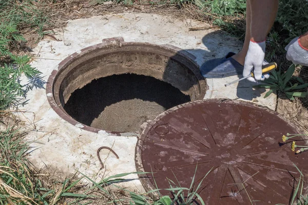 Adam kuyunun rögar kapağını açtı. Su sayacı denetleniyor ve yükleniyor.