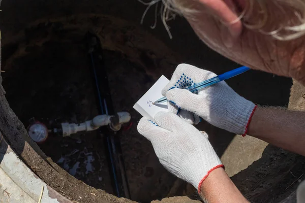 Man Registrerar Avläsningarna Vattenmätaren Lutande Över Brunnen Kontroll Och Bokföring — Stockfoto