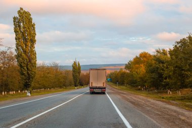 Yarı karavan kamyonu bir sonbahar günü ağaçların arasında yol alır. Kargo taşımacılığı ve lojistik.