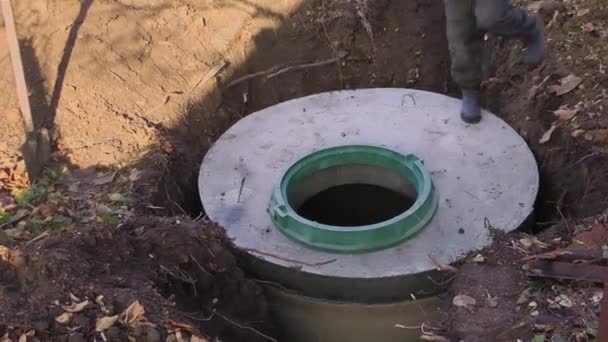 Рабочий устанавливает канализационный люк на септик из бетонных колец. Строительство канализационных сетей для загородных домов — стоковое видео