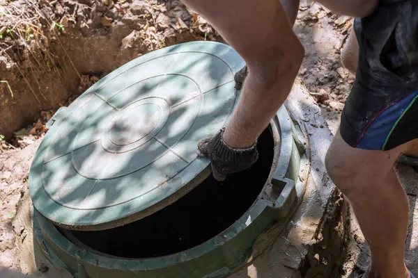 Adam kanalizasyon kapağını açıyor. Septik tankların kurulumu ve bakımı.