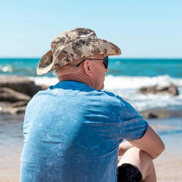 Ένας Ηλικιωμένος Κάθεται Στην Παραλία Μια Ηλιόλουστη Καλοκαιρινή Μέρα Και — Φωτογραφία Αρχείου