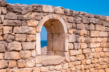 Antik taş duvar kemerli ve deniz manzaralı.