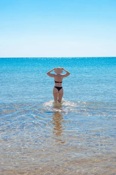 Dojrzała szczupła kobieta w stroju kąpielowym wchodzi do morza z tyłu. Wakacje, podróże i turystyka — Zdjęcie stockowe