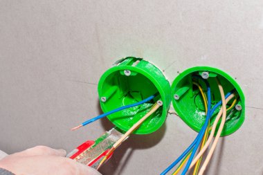 Bir elektrikçi elektrik prizi kurmak için alçıpan duvarına bir çıkış kutusu yerleştirir. Ev yenilenmesi.