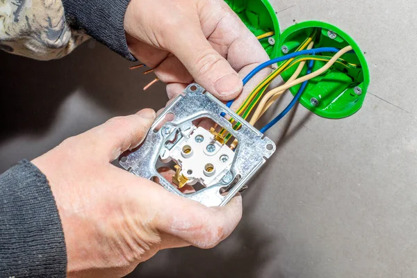 An electrician installs an electrical outlet into a drywall wall. Carrying out electrical wiring to the house.