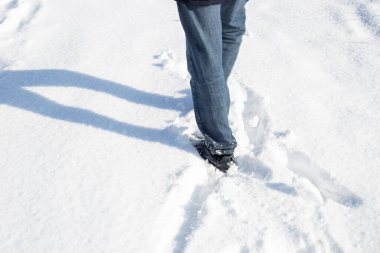 Kotlu ve spor ayakkabılı bir adam kış günü beyaz pofuduk kar içinde yürür..