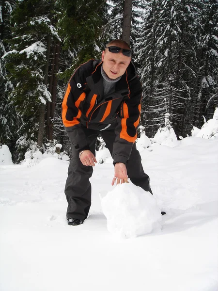 Egy fiatal férfi sculpts snowball a hegyek a háttérben — Stock Fotó