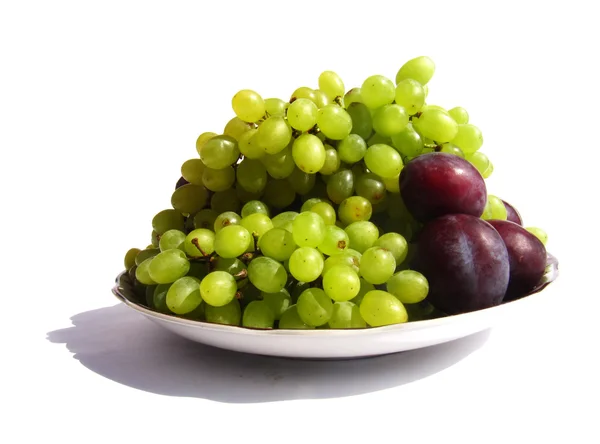 Green grapes and three plums on a plate isolated on white backgr — Stock Photo, Image