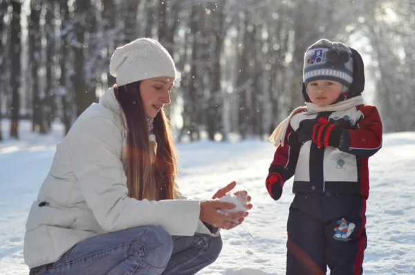 Young mother making snowballs for a kid on a winter walk in the — Stock Photo, Image
