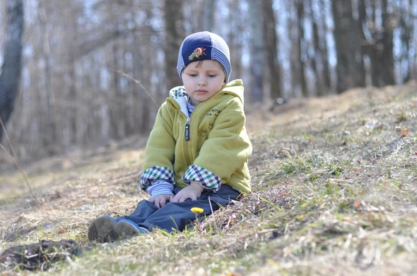 Baby sitting on spring grass and views the first flowers — Stock Photo, Image