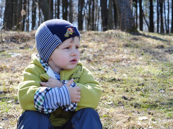 Kid with a deep thoughtful look sat on spring grass — Stock Photo, Image