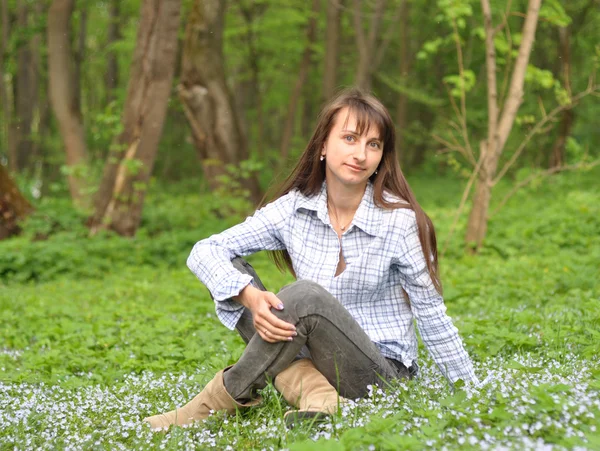 Mooie lachende jonge vrouw zittend op het gras in het park — Stockfoto