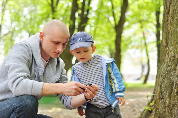 Dzieci z zainteresowaniem patrząc na telefon tatusia w parku — Zdjęcie stockowe