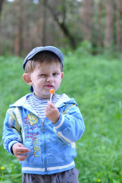 Copilul mănâncă bomboane pe un băț cu o privire nemulțumită pe față — Fotografie, imagine de stoc