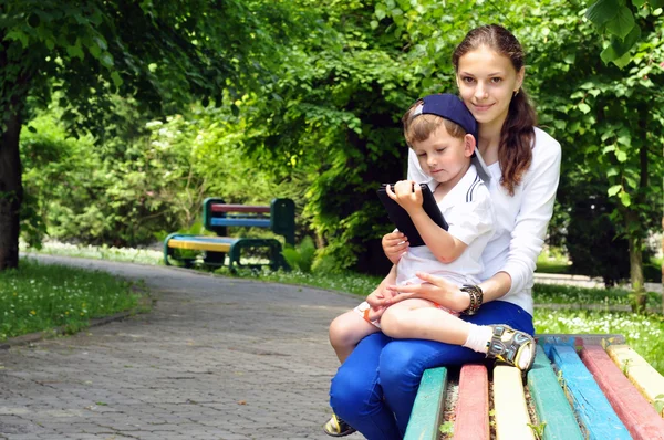 Děti sedí na lavičce v parku hrát tabletu — Stock fotografie