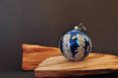 Ahşap bir tahtada duran gümüş parıltılı mavi bir Noel balosu. Kapatın, mesajınız için boş yer var.