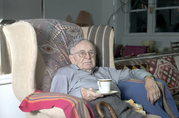 Senior man sitting on couch with cup — Stock Photo, Image