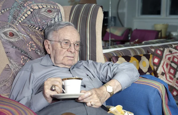 Senior man sitting on couch with drinking cup — Stock Photo, Image