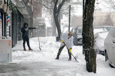 BRONX, NEW YORK, ABD - 29 Ocak 2022: İspanyol erkekler kar fırtınası sırasında berber işleri önünde kar kürüyorlar.