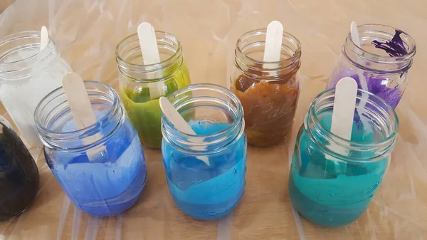 Mixing acrylic paint with floetrol for flow painting. mason jars with acrylic paint colorful colors from peacock feathers.