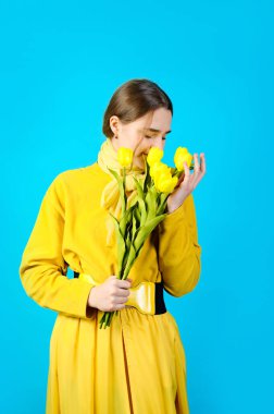 Elinde sarı lale çiçekleri olan genç bir kızın portresi. mavi arkaplan