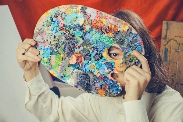 Elinde palet tutan bir sanatçının yüzü kapalı.