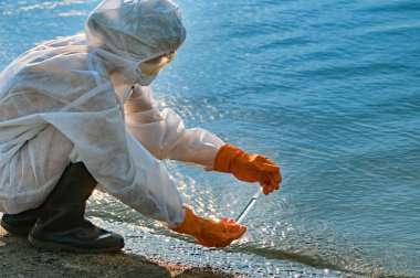 Koruma giysisi ve maskesi olan bir uzman tarafından suyu kontrol ediliyor.