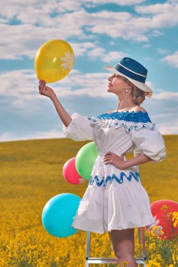 Tarlada balonları olan şapkalı güzel bir kadın.