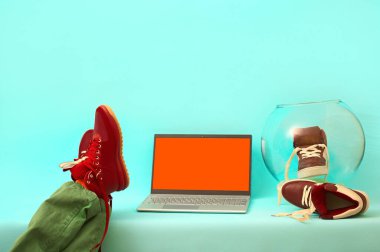 Adam bacakları masada dinleniyor. Mavi arka planda gümüş dizüstü bilgisayar