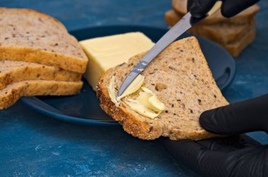 Eldivenli şef bir dilim ekmeğin üzerine bıçakla tereyağı sürer.