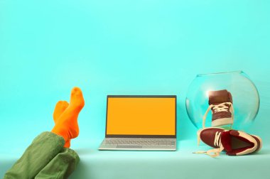 Adam bacakları masada dinleniyor. Mavi arka planda gümüş dizüstü bilgisayar