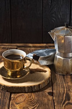 Altın fincanda sade kahve. Kahve demliği ve dökülen bir poşet kahve.